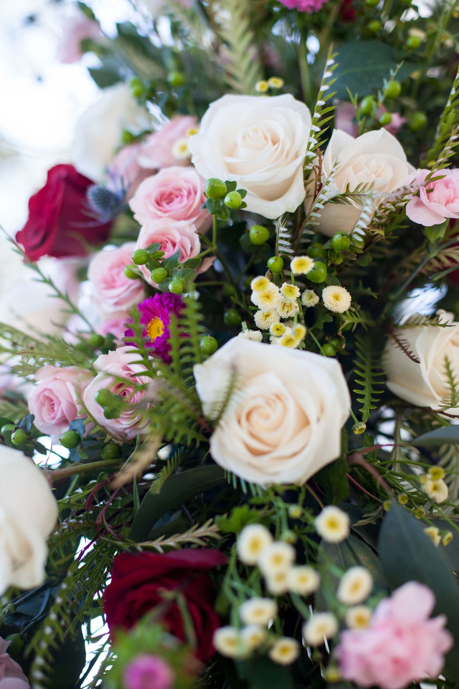 Beautiful floral arrangement featuring white and pink roses with burgundy accents and delicate yellow blooms among green foliage.