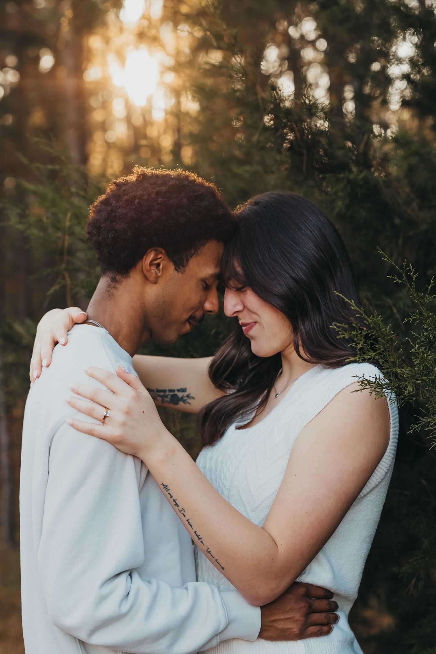 Couple shares an intimate forehead-to-forehead moment during a golden hour engagement session in pine trees.