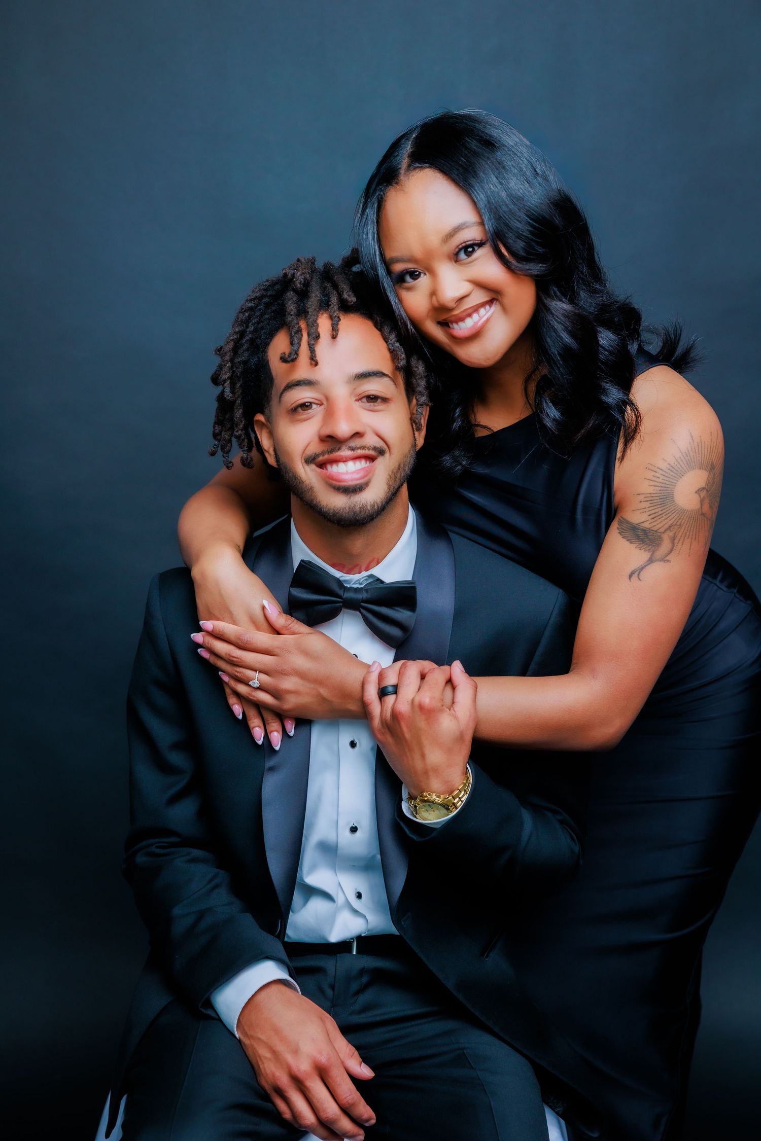Smiling engaged couple in black formal attire pose together during studio engagement photography session.