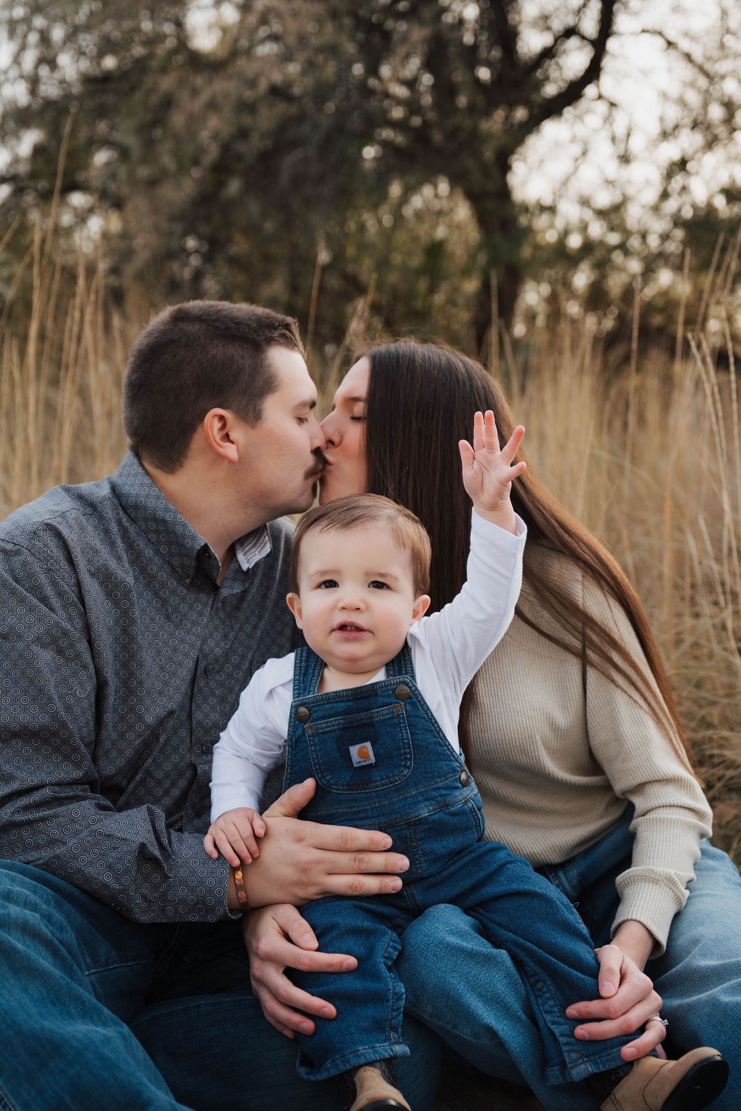 A family shares tender moments together outdoors in a field of tall grass during a photo session.