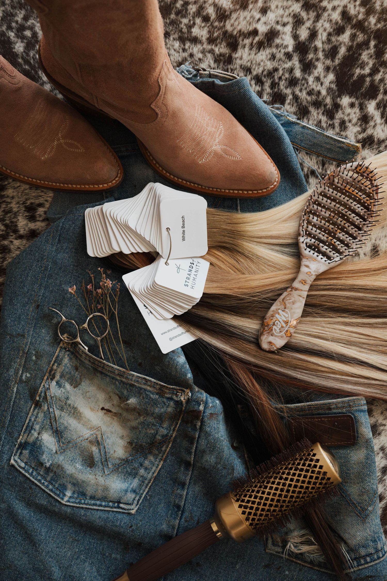 Flat lay of western-style accessories including boots, denim, and hair tools.