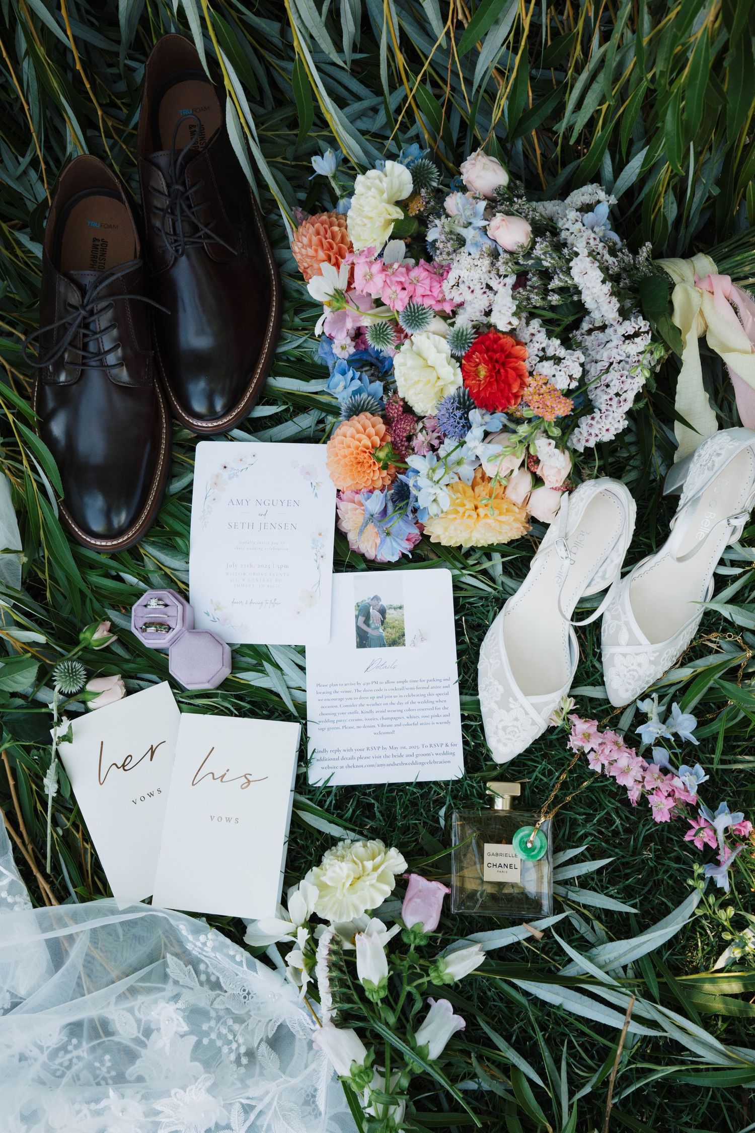 Wedding details including delicate lace shoes, handwritten notes, and colorful floral arrangements laid out on grass.