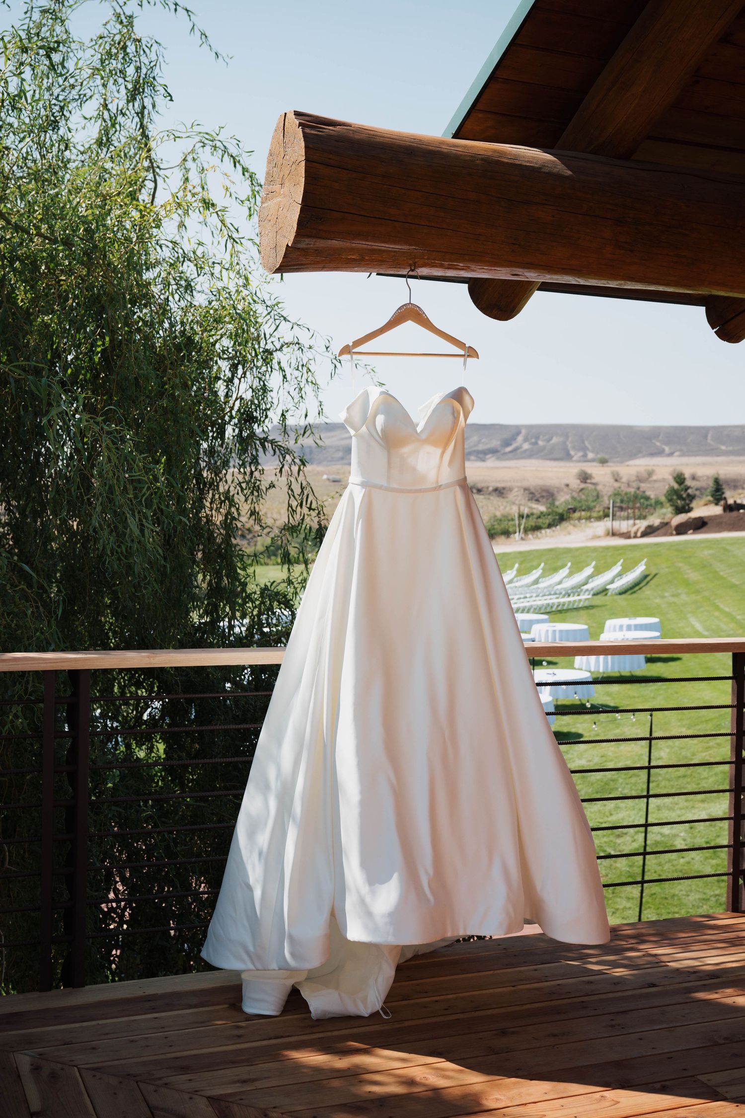 An elegant white wedding dress hangs on display against a scenic outdoor backdrop.