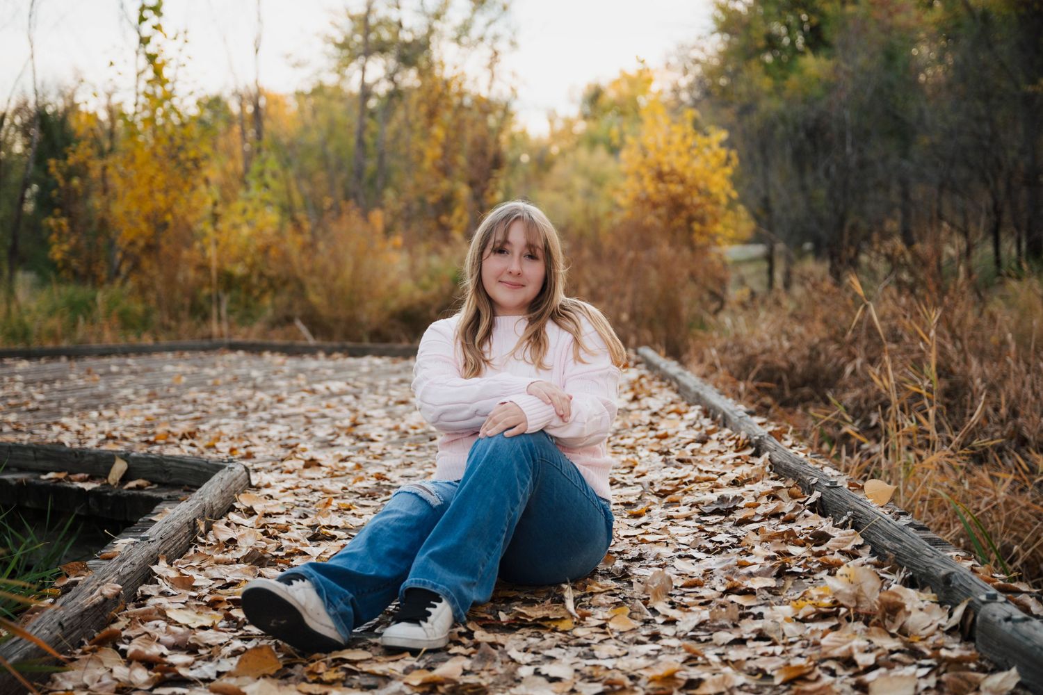 Fall foliage surrounds a rustic wooden path covered in fallen leaves.
