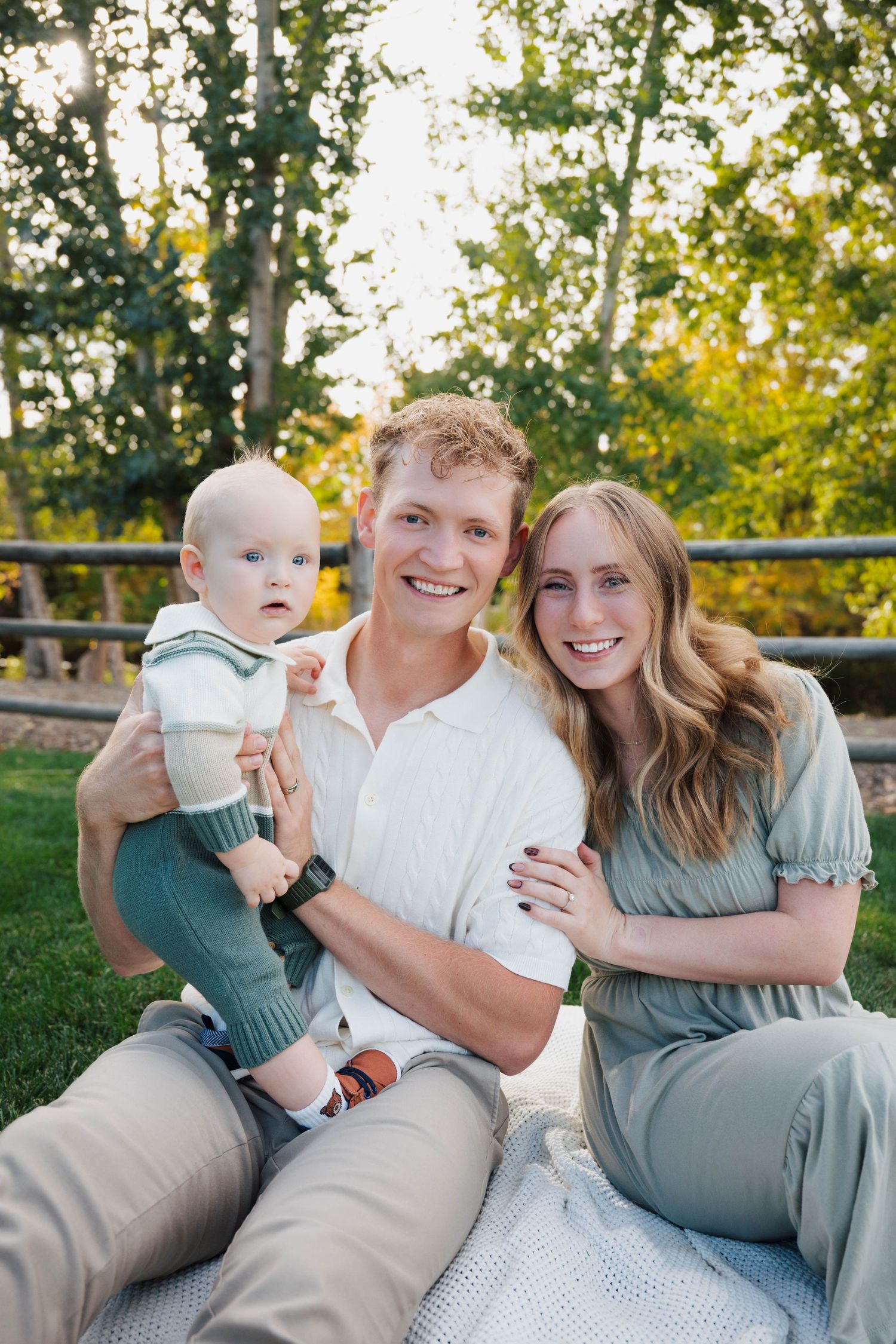 A family in coordinating sage green and white outfits poses together outdoors during a sunset photo session.
