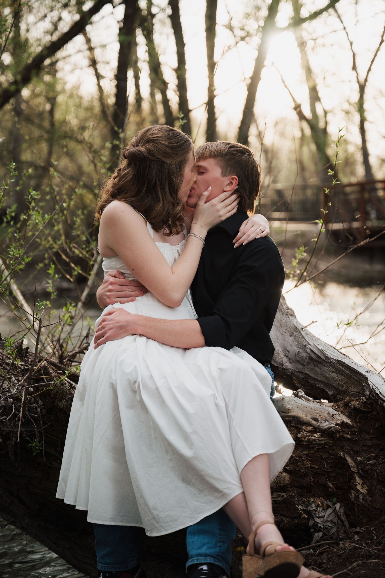 Romantic couple poses on fallen log during forest photoshoot.