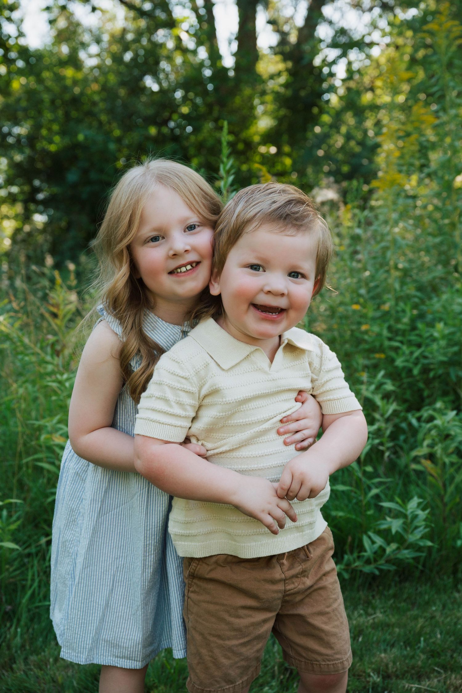 Two young children share a joyful embrace while playing outdoors in a natural garden setting.