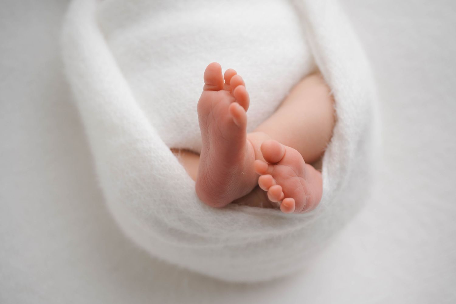 Close-up of newborn baby feet wrapped in a soft white blanket, showcasing tiny toes and delicate skin.