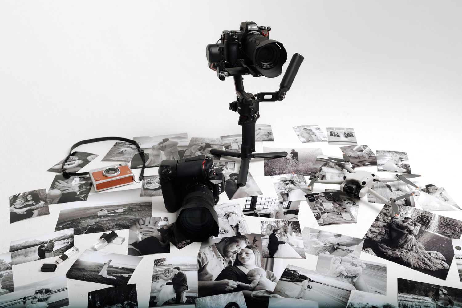 A camera on a gimbal stabilizer surrounded by scattered black and white photographs on a white surface.
