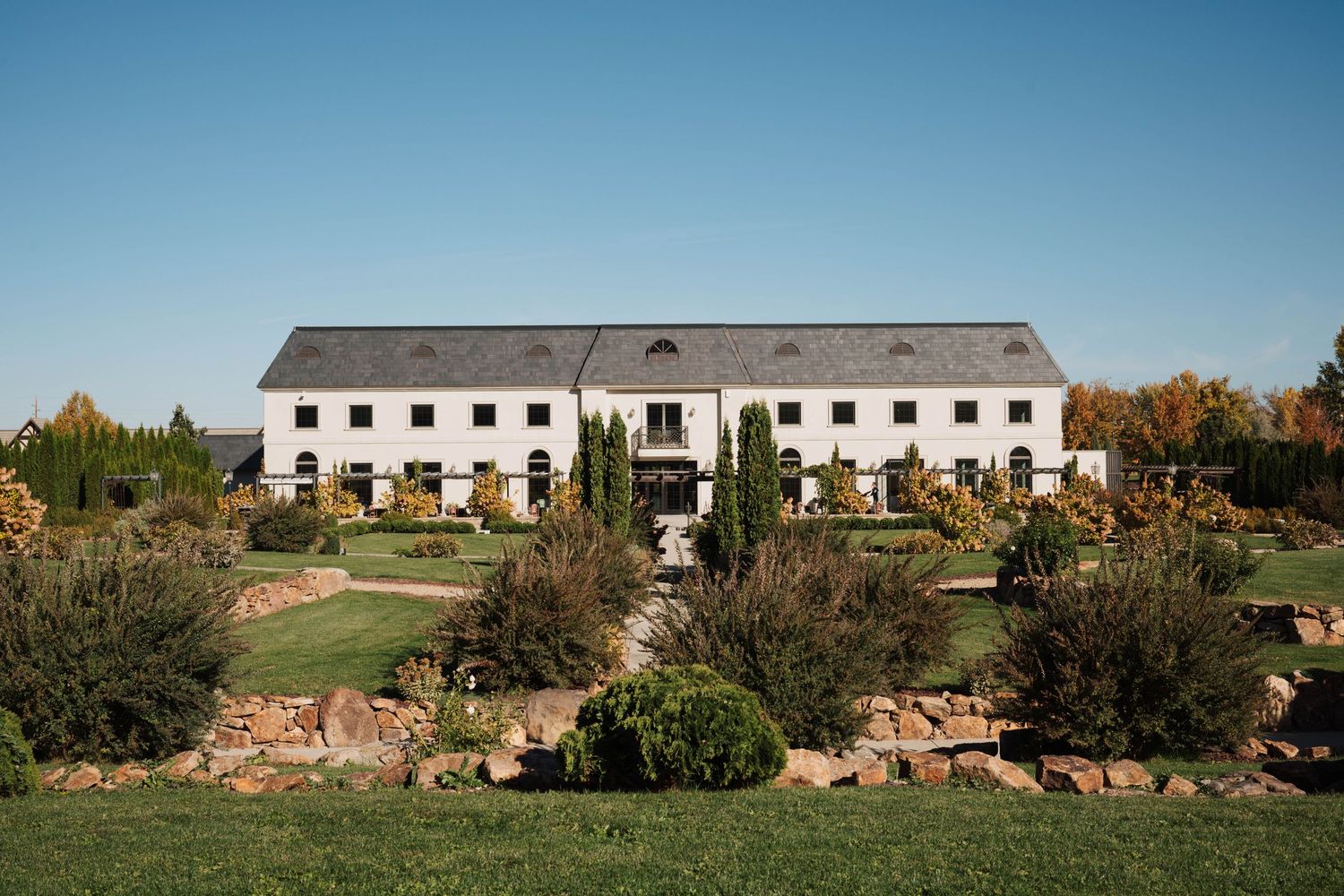 Panoramic view of a white farmhouse building with multiple connected sections nestled in a rural countryside setting.