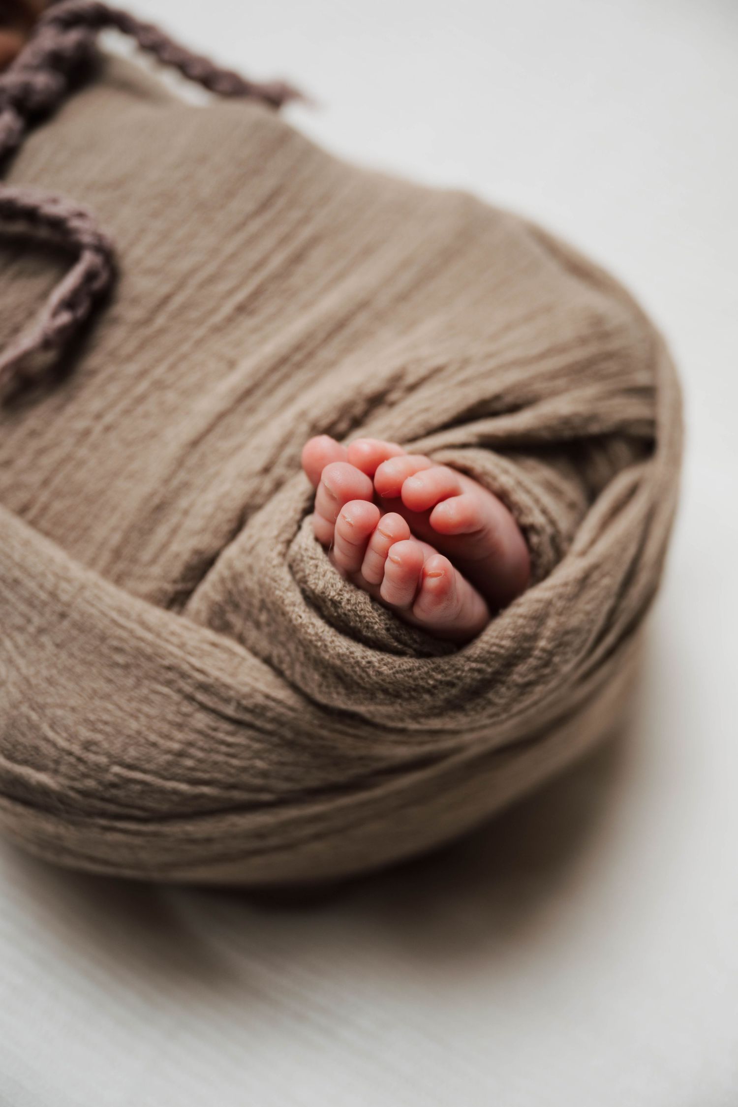 Close-up view of tiny baby toes peeking out from a brown swaddle wrap against a white surface.