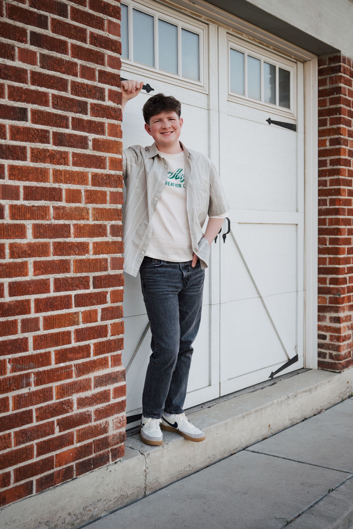 Casual pose against white garage door and red brick wall.