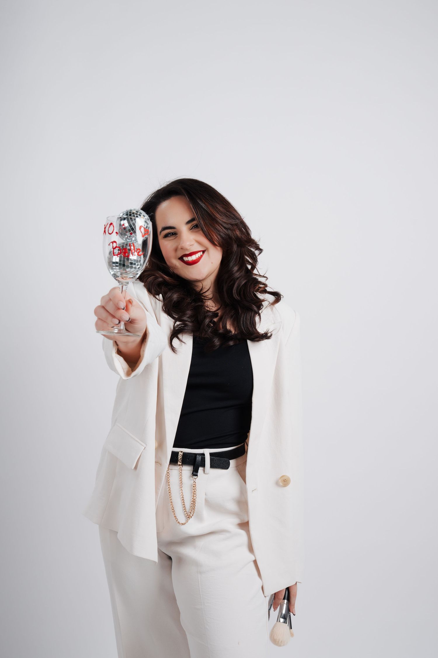 Woman in white blazer and black top posing with disco ball against white background.
