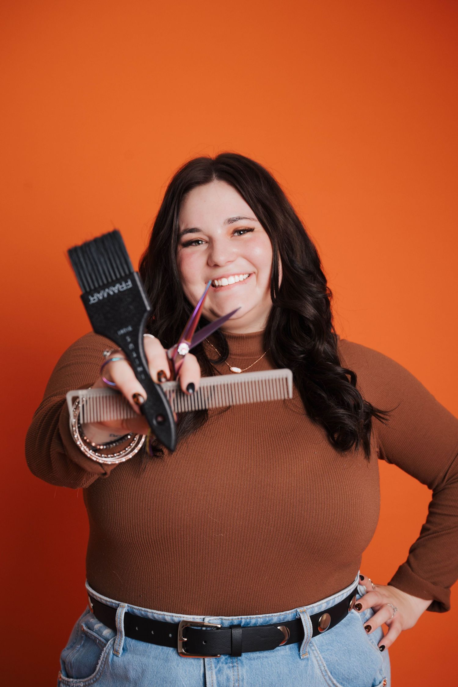 Hairstylist displaying various styling tools against an orange background.