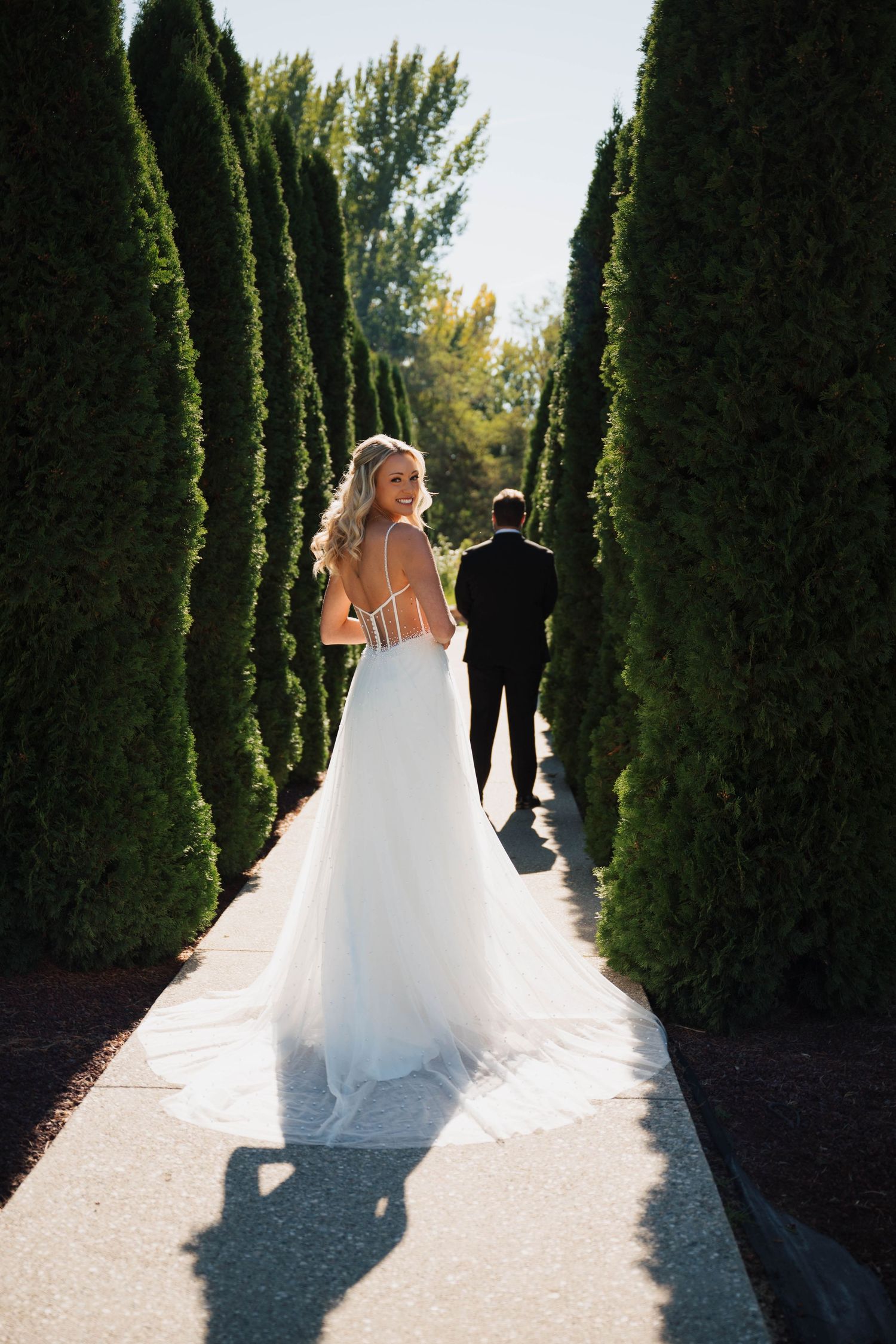 Wedding couple walking down cypress tree-lined path creating dramatic shadows.