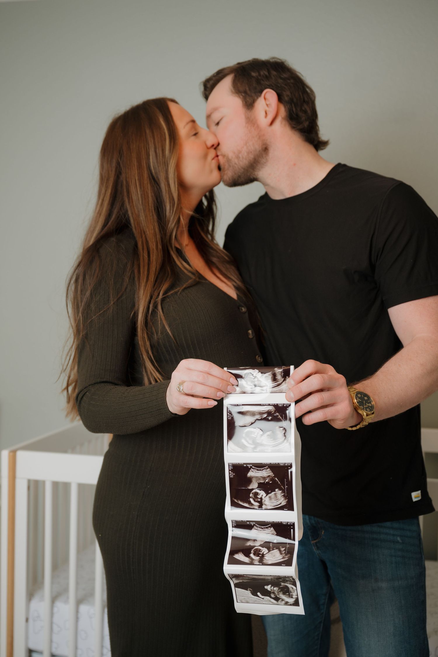 Couple shares intimate moment while holding ultrasound photos in nursery.