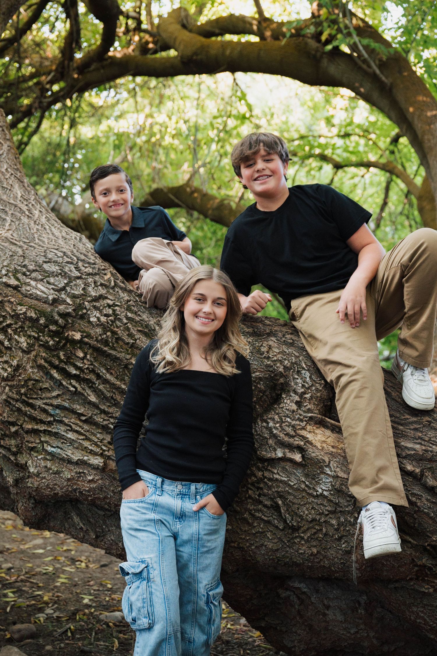 Candid family photos of people sitting and posing on a large tree branch in a natural setting.
