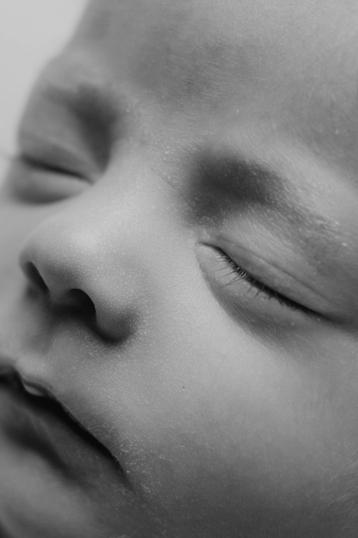 Close-up black and white portrait of a sleeping newborn baby with delicate features and soft skin.
