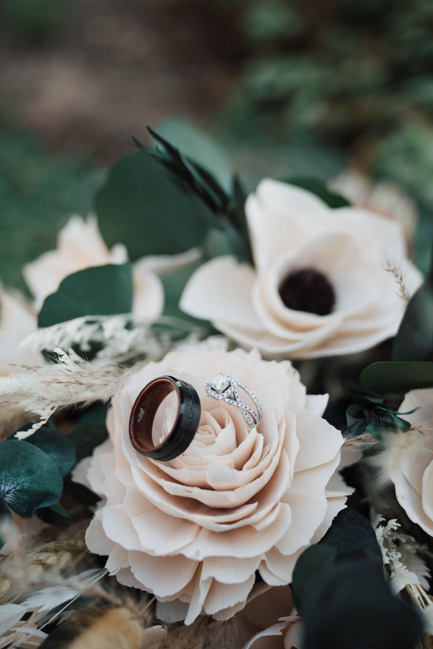 Wedding rings nestled in a cream-colored rose with green foliage background.