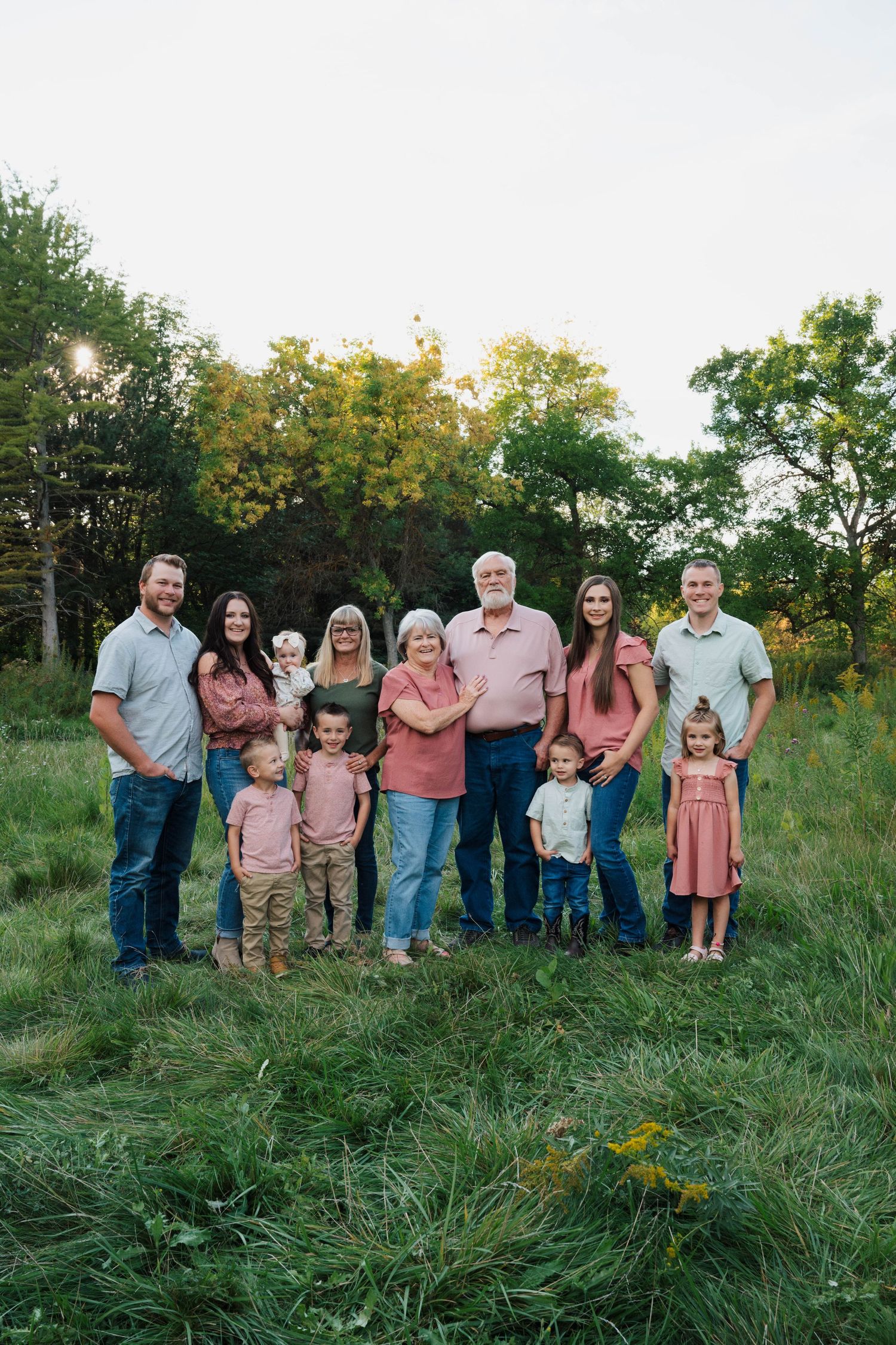 Large family group posed together on grassy hillside in coordinated casual outfits.