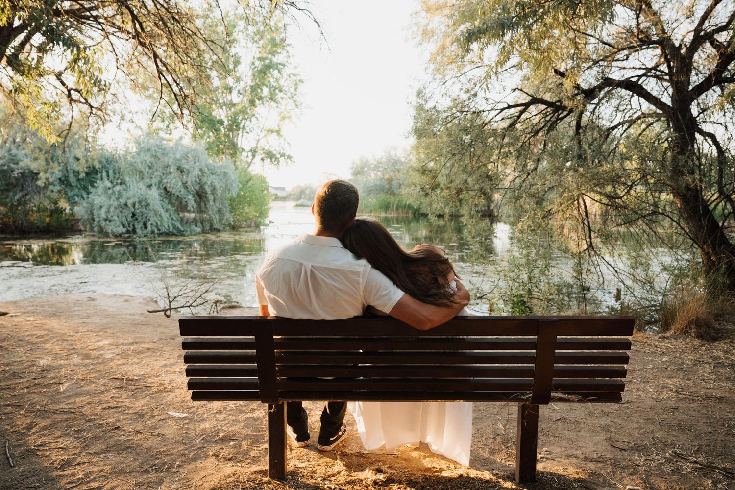Couple sitting together on wooden bench during sunset by waterfront.