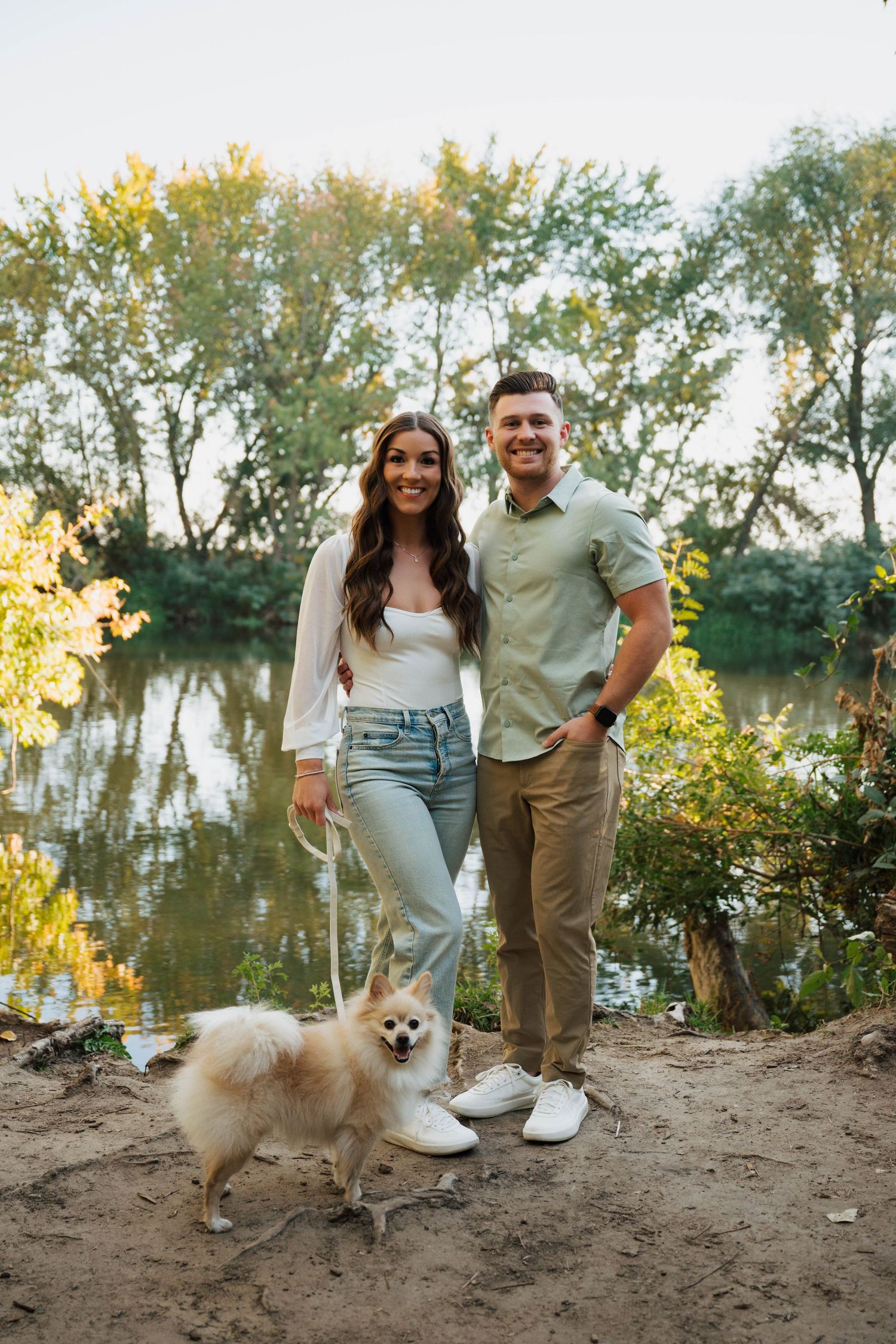 A couple walks along a lakeside trail with their fluffy Pomeranian dog.
