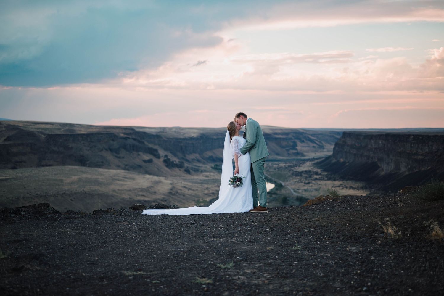 A bride and groom share a romantic kiss on a dramatic canyon overlook at sunset during their outdoor elopement.