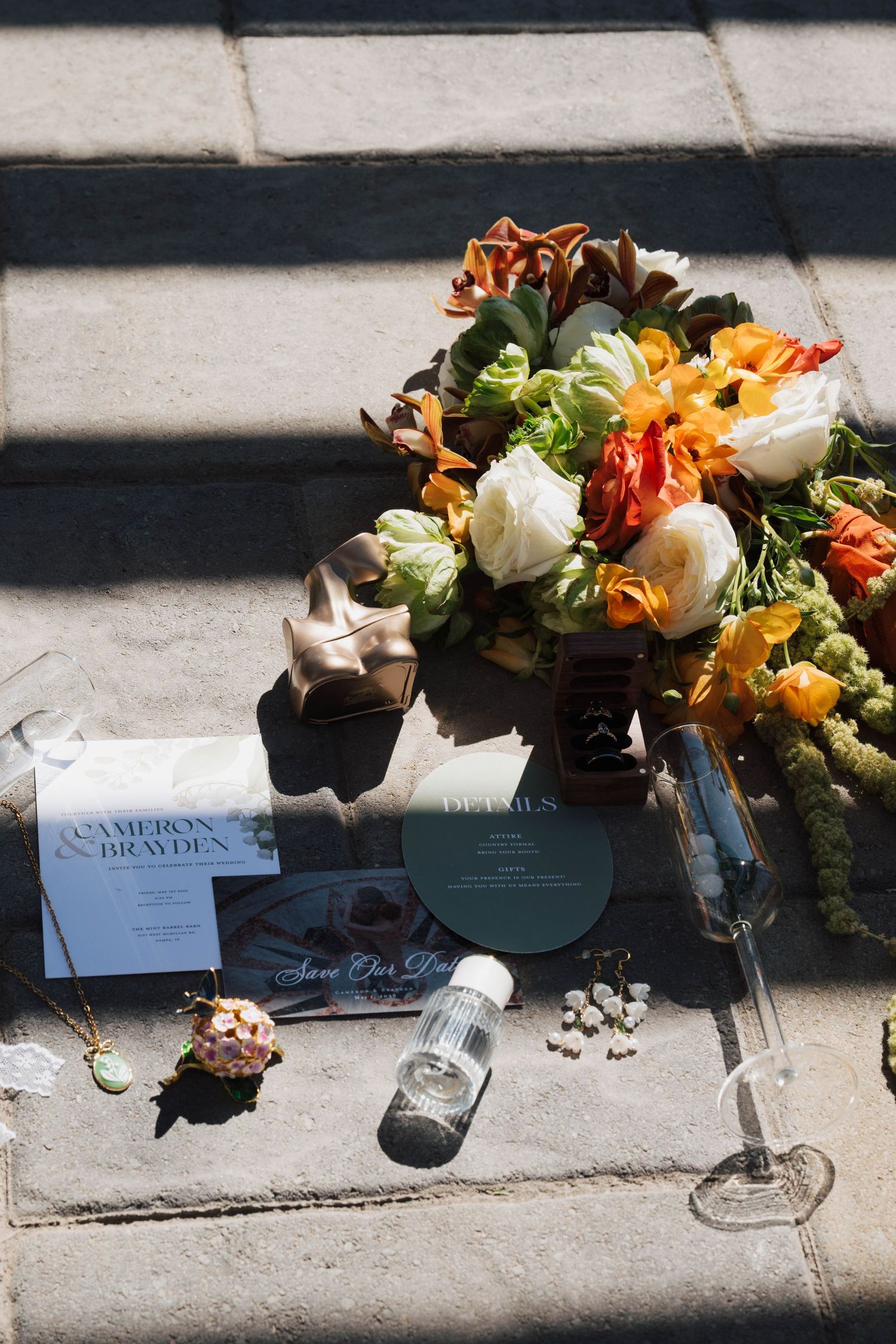 Wedding flat lay with colorful bouquet, save the date cards for Cameron & Brayden, champagne flute, and small gifts on stone.