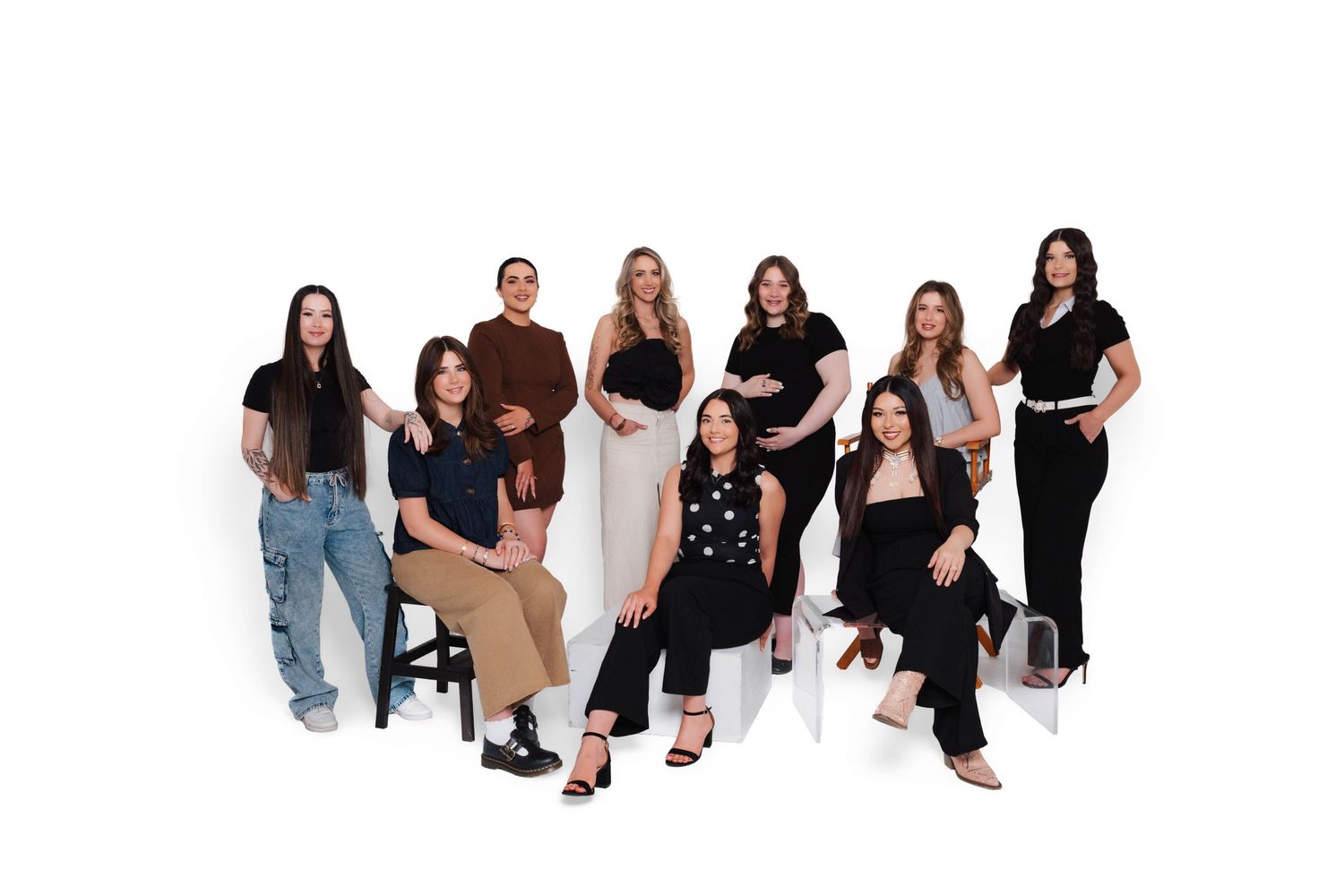 A professional group photo of nine women posing together against a white background in stylish outfits.