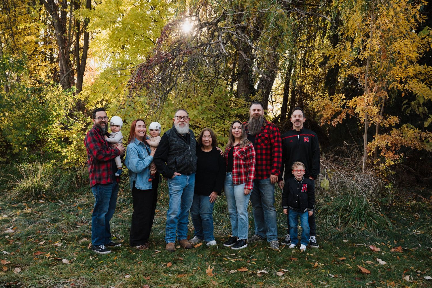 Family members in casual attire pose together against an autumn backdrop with golden leaves.