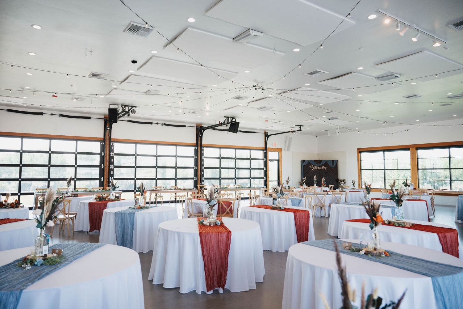 Modern banquet hall setup with round tables and white linens in a bright room with large windows and waterfront views.