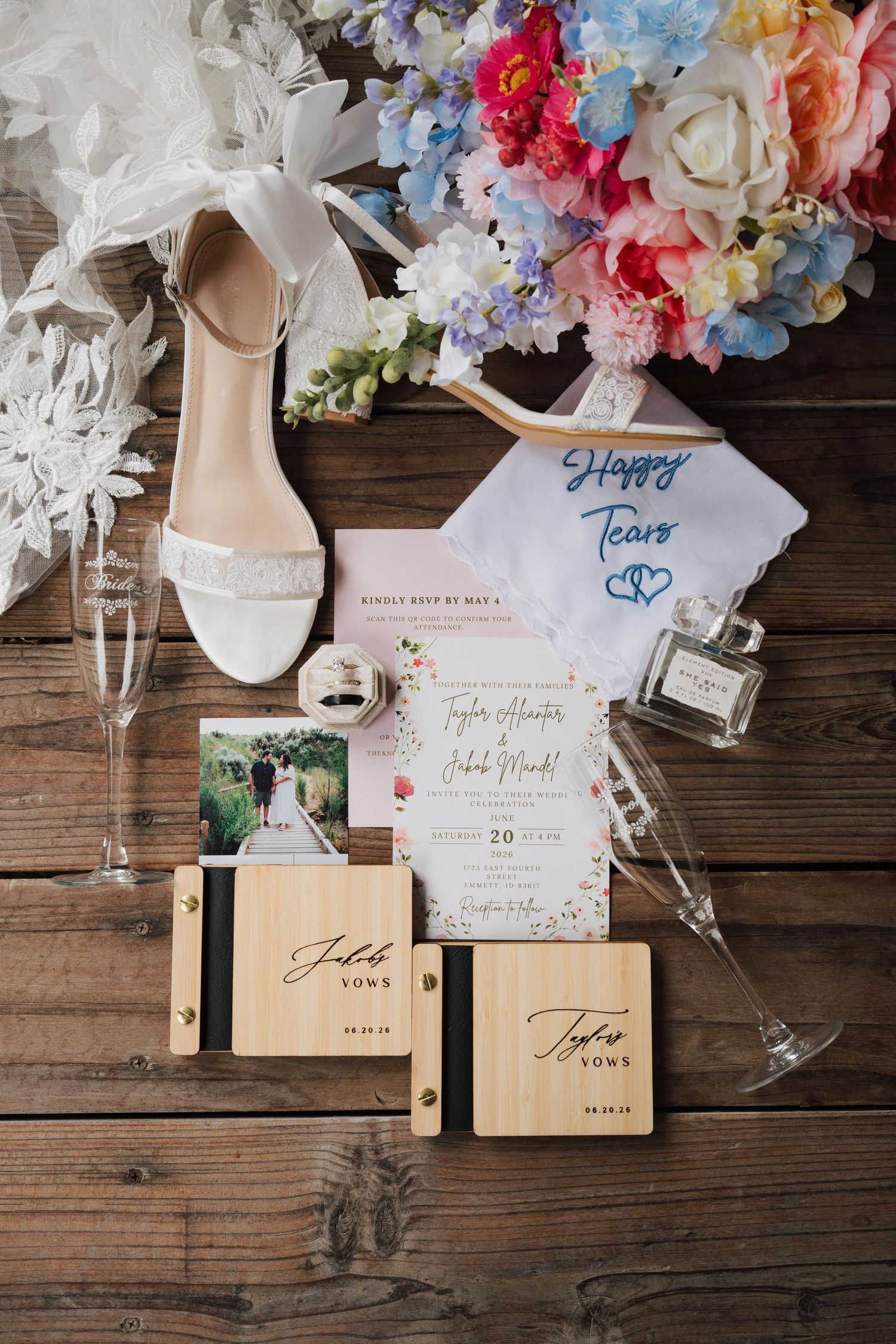 Elegant wedding flat lay with bridal heels, floral bouquet, vow books, champagne flutes, and colorful wedding invitation on wood.