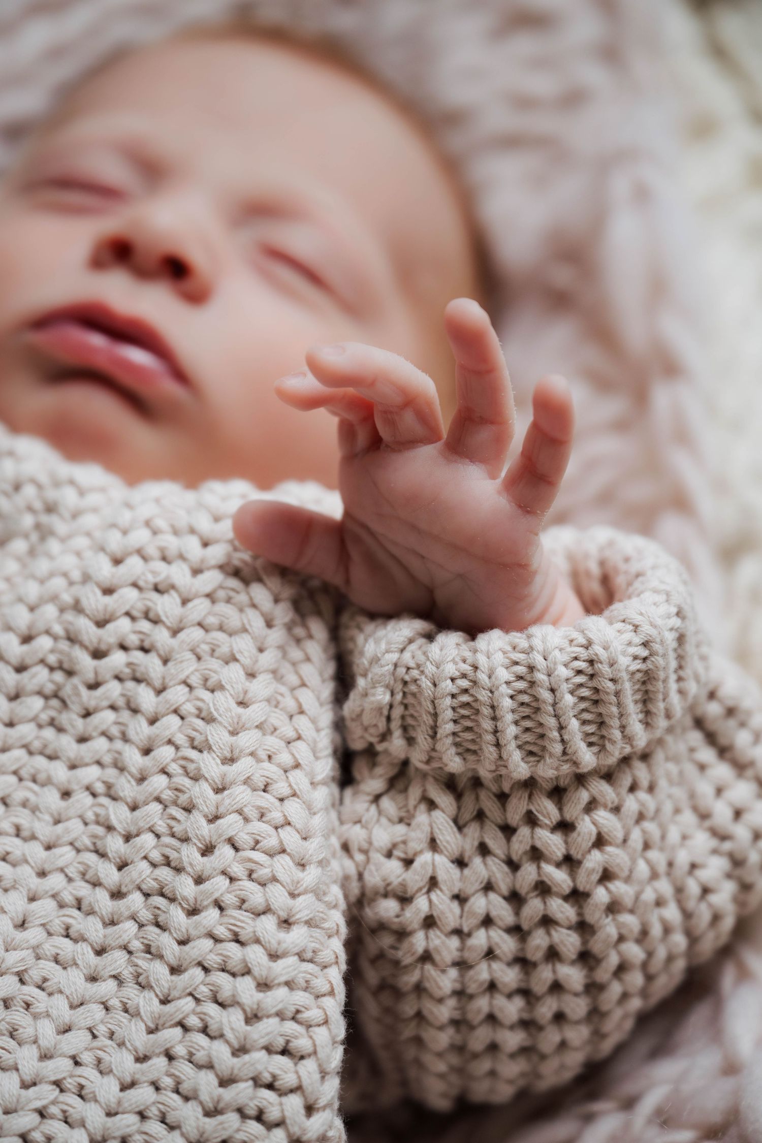 Close-up of newborn baby's hand against knitted cream blanket texture.