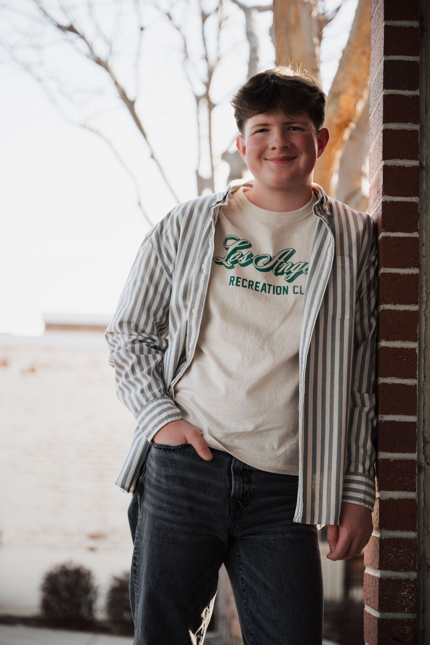 Casual portrait by brick column featuring striped shirt and branded t-shirt combination.
