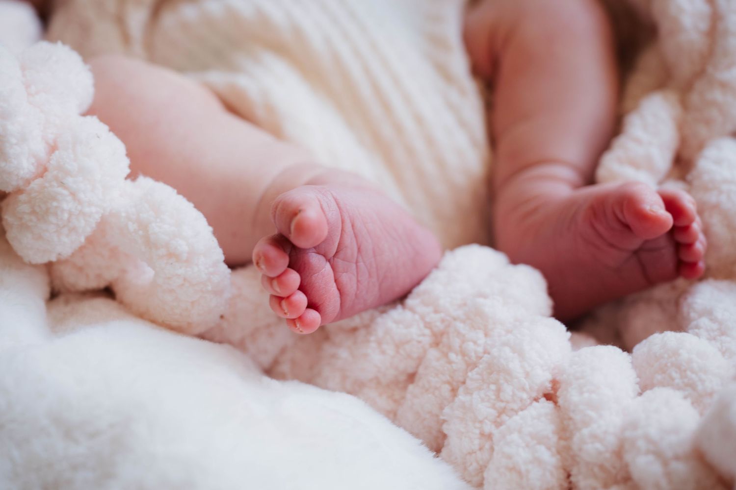 Close-up of tiny newborn feet against soft white textured blanket.
