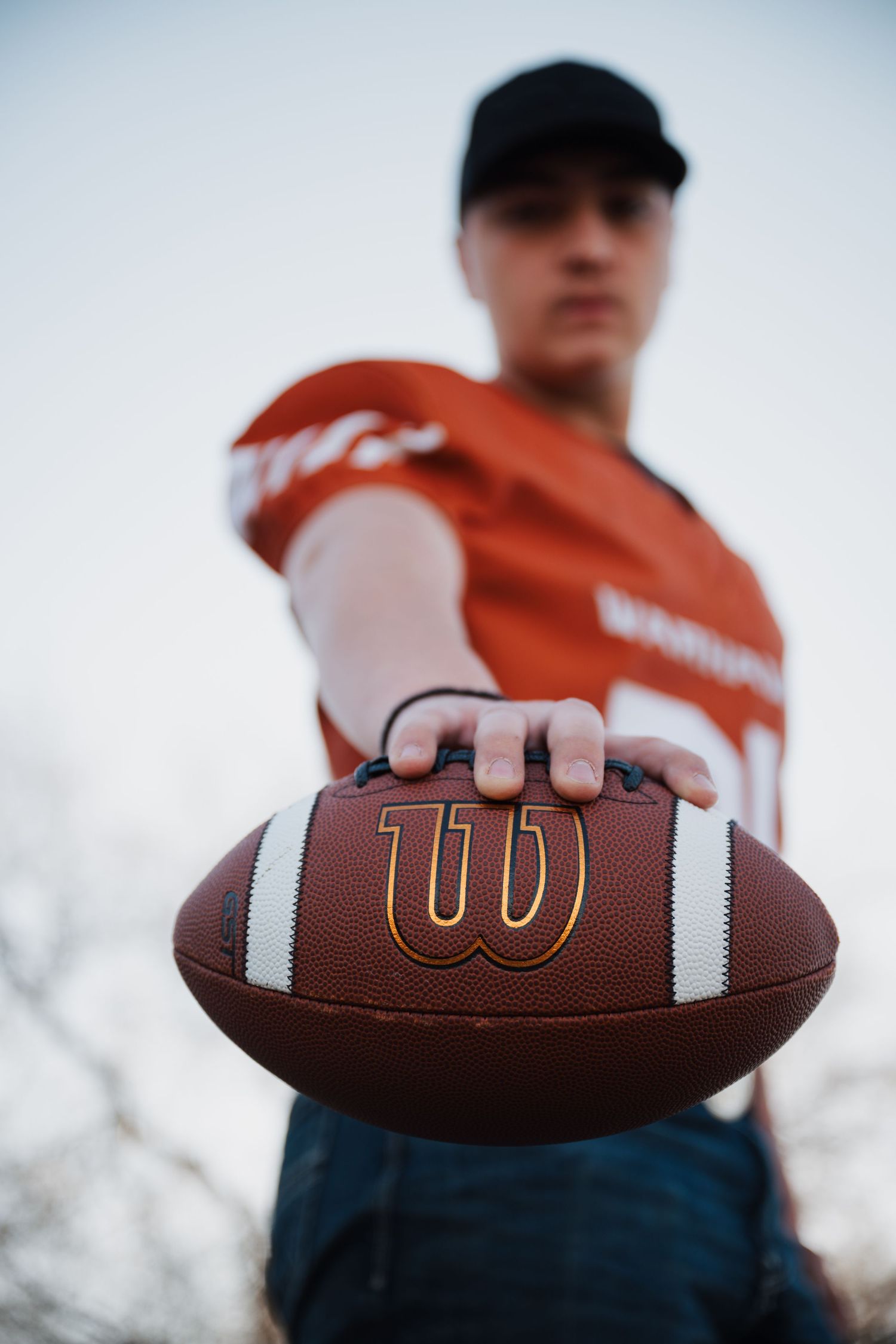 Close-up of Wilson football being held out by player in orange sports jersey.
