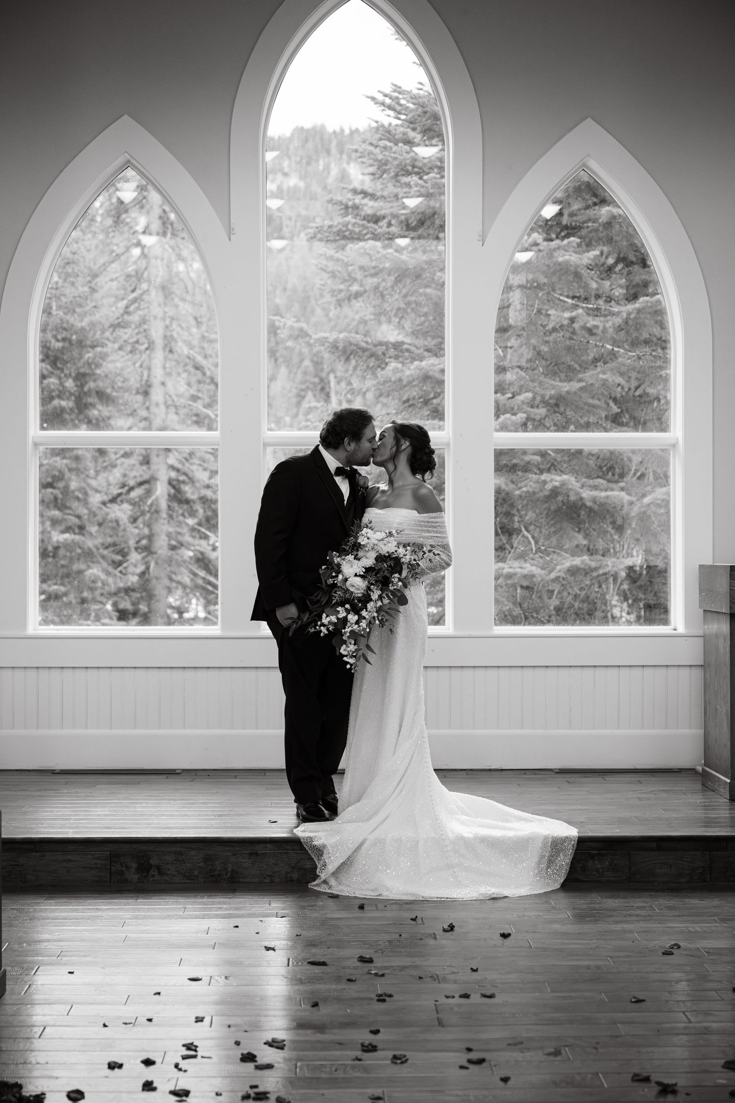 An elegant wedding scene unfolds in a bright chapel with gothic windows and scattered rose petals.