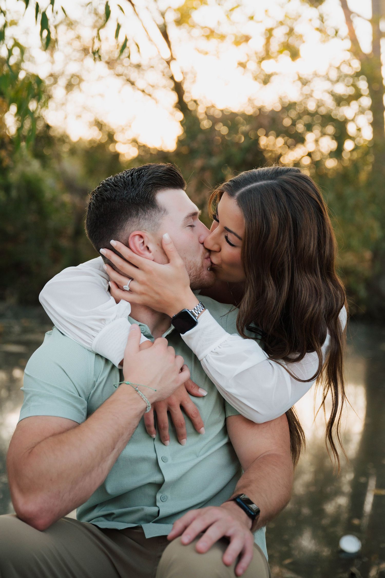 A couple shares a romantic moment on grass near a lake during golden hour.