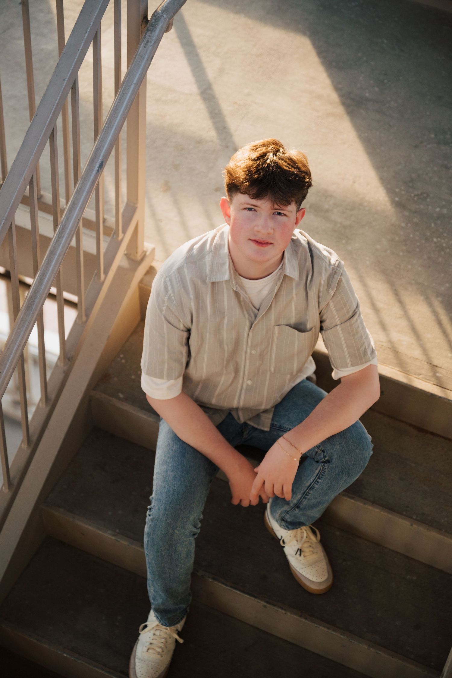 Natural light portrait on stairs showing casual style with button-down shirt and denim.