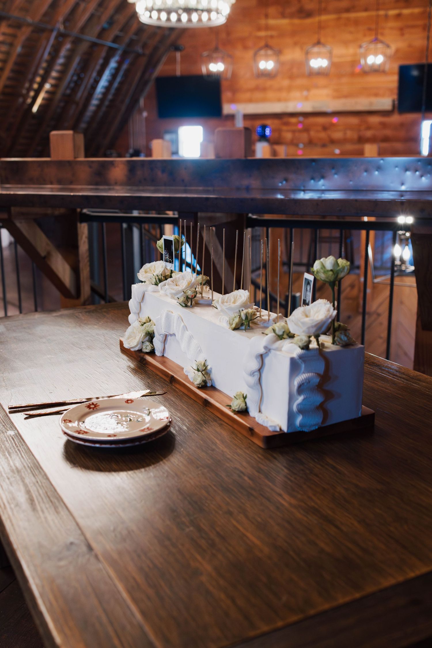 Rustic barn wedding reception table with white floral centerpiece and place settings on wooden table.