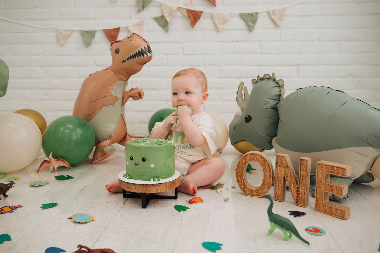 Dinosaur-themed first birthday setup with green cake, balloons, and decorative elements.