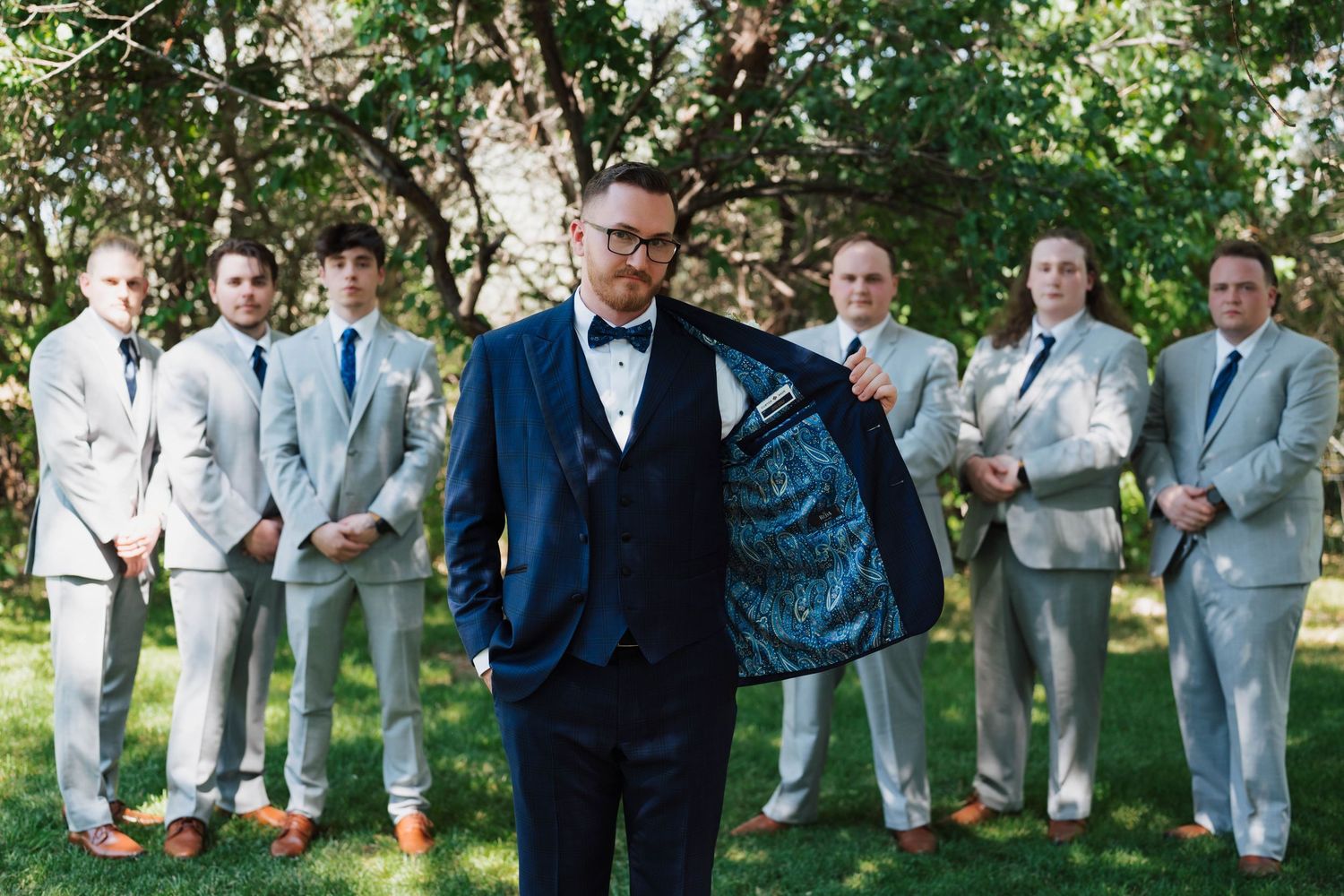 Groom in navy suit showing blue floral lining with groomsmen in gray suits standing outdoors.