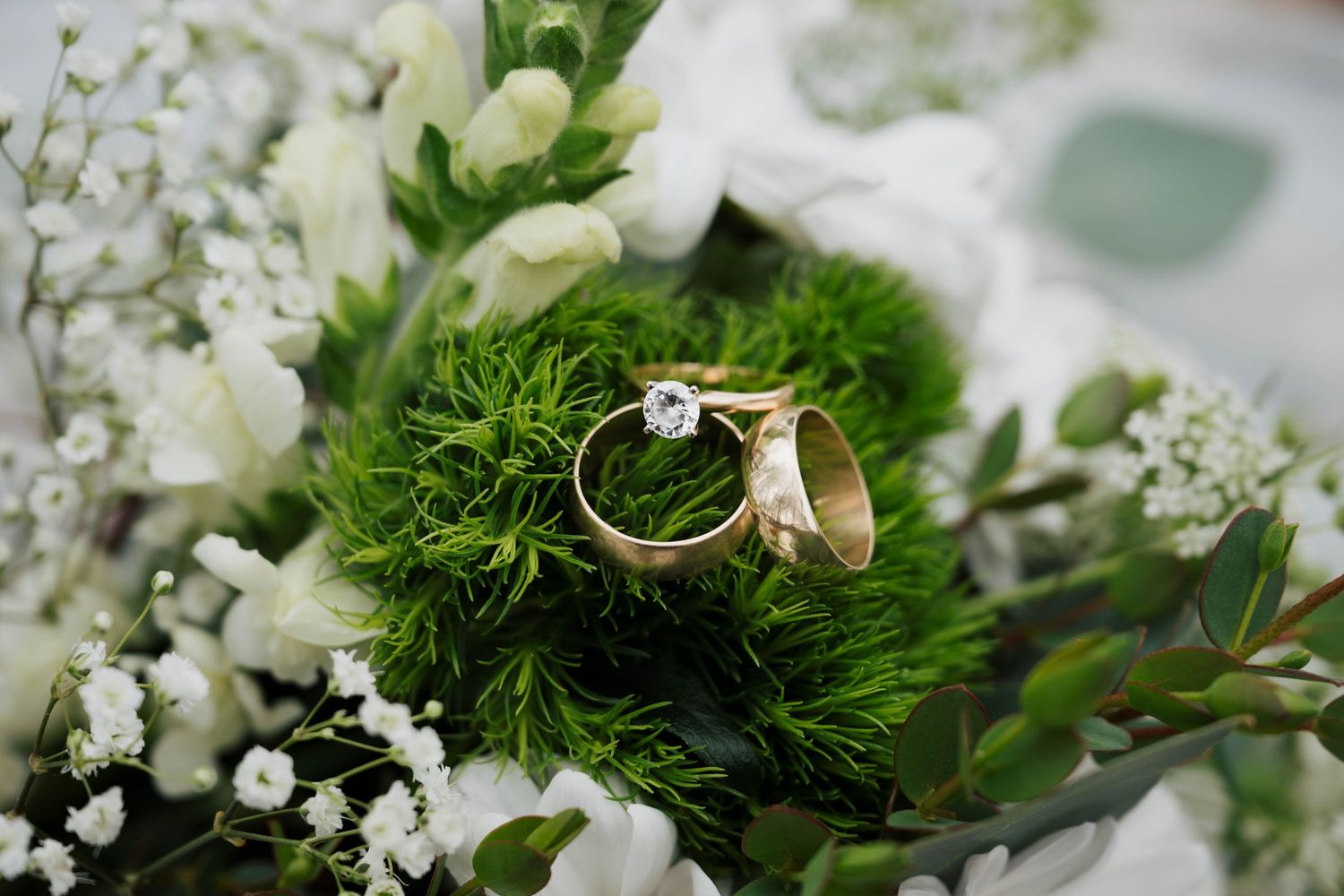 Wedding rings rest on fresh green moss with delicate white flowers and floral decor.
