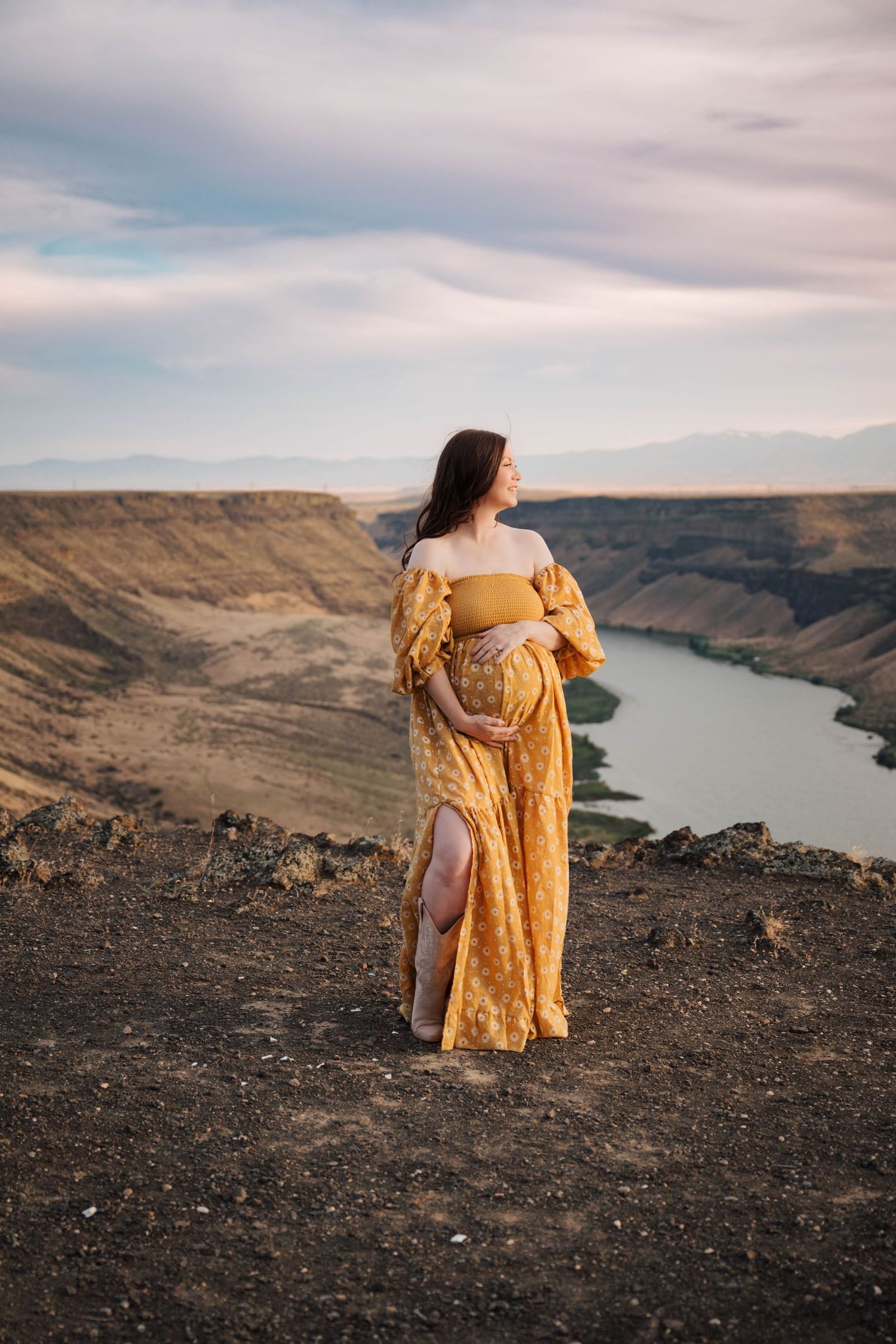 A yellow dress flows in the wind against dramatic canyon and river landscape.
