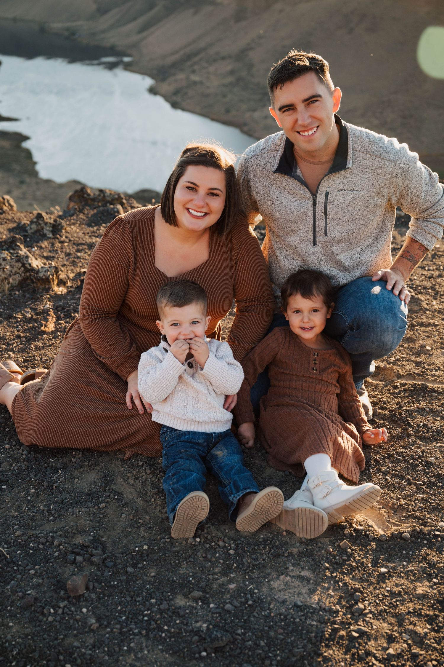 Family sits together on rocky terrain during sunset photo session.