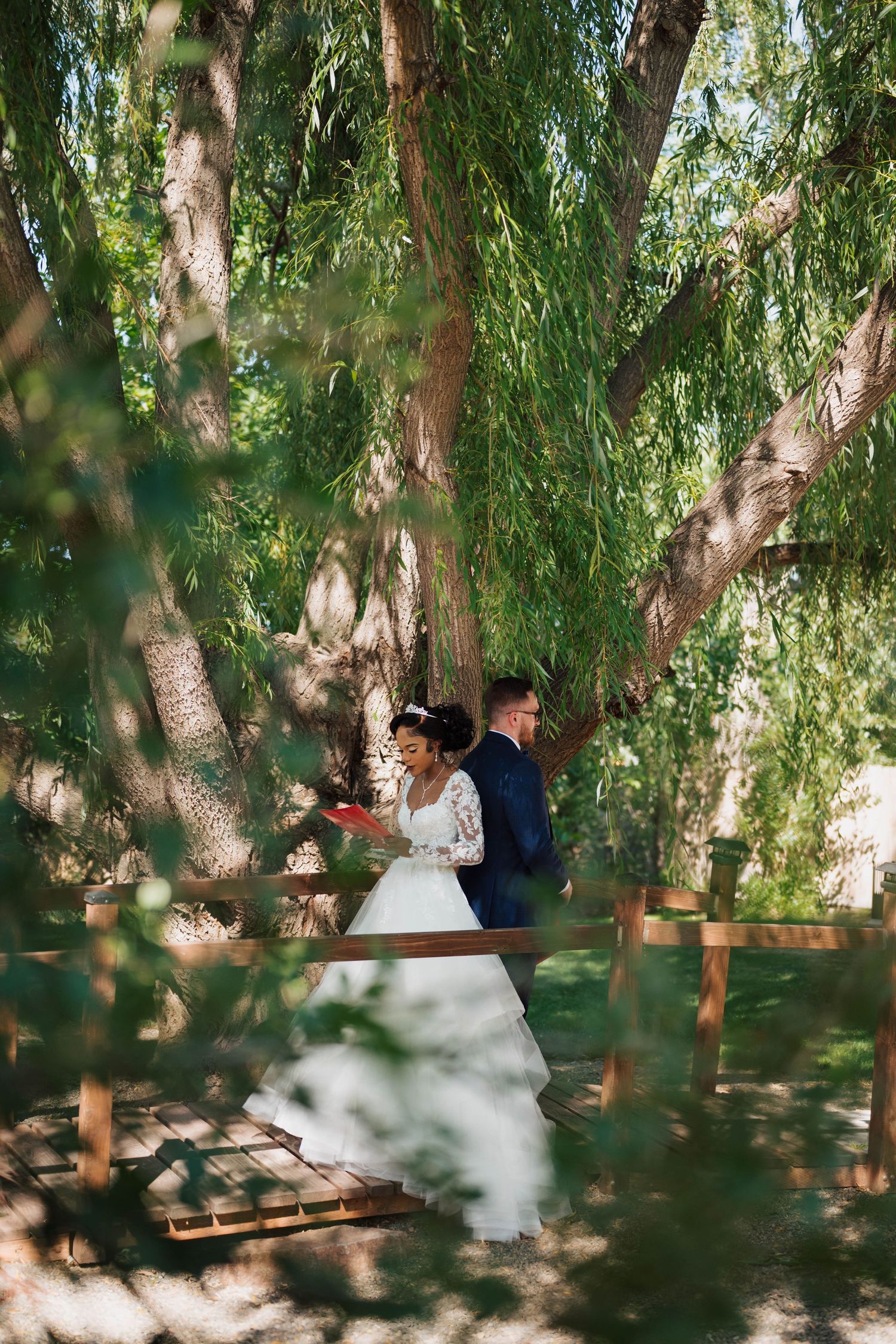 Bride and groom exchange vows under a large willow tree at an outdoor wedding ceremony.