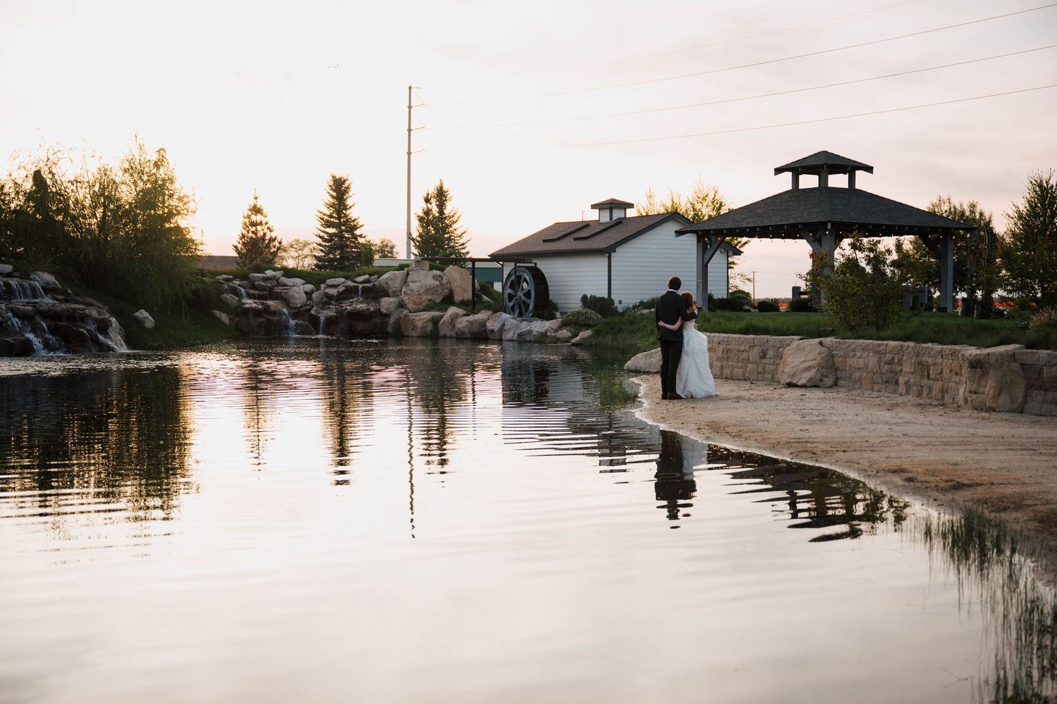 A bride and groom share a romantic moment by a reflective pond at golden hour near a white mill wedding venue.