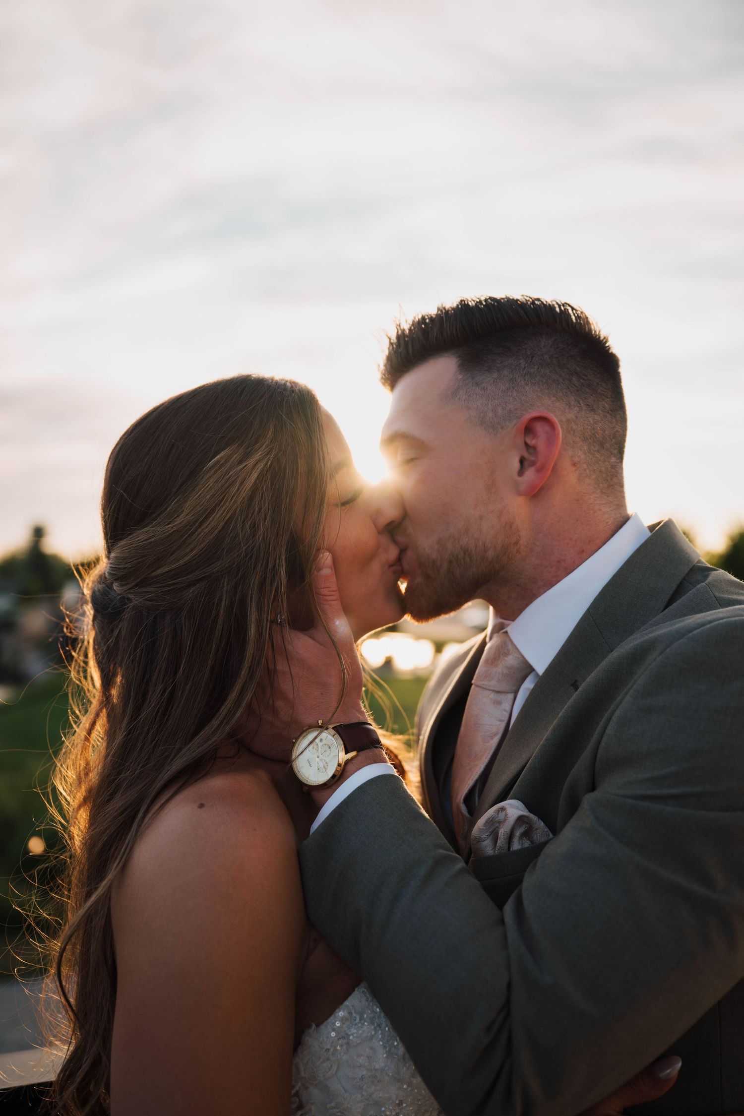 A bride and groom share a romantic sunset kiss, with golden backlight illuminating their wedding attire.