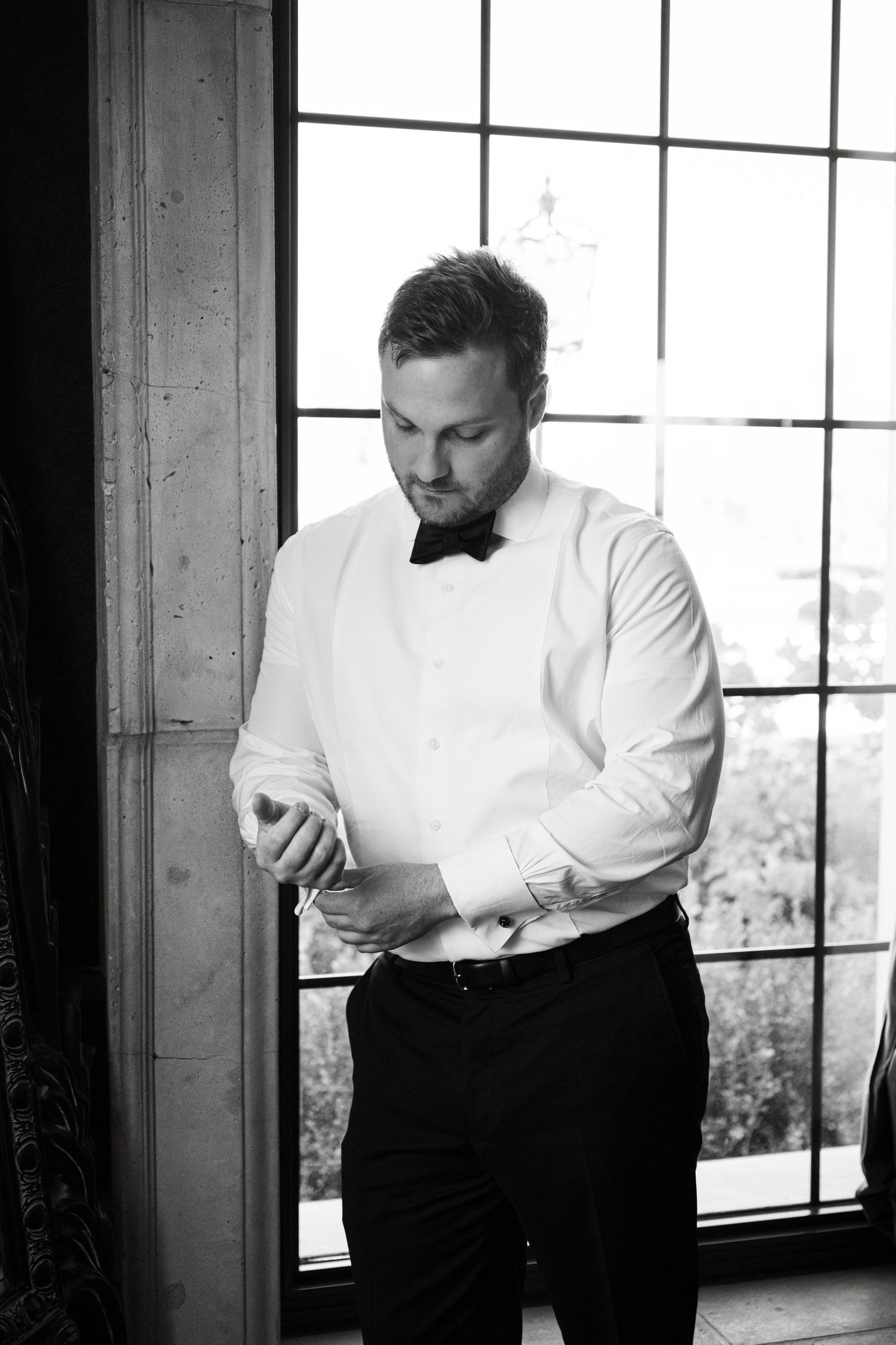 Classic black and white getting ready shots of groom adjusting formal attire.