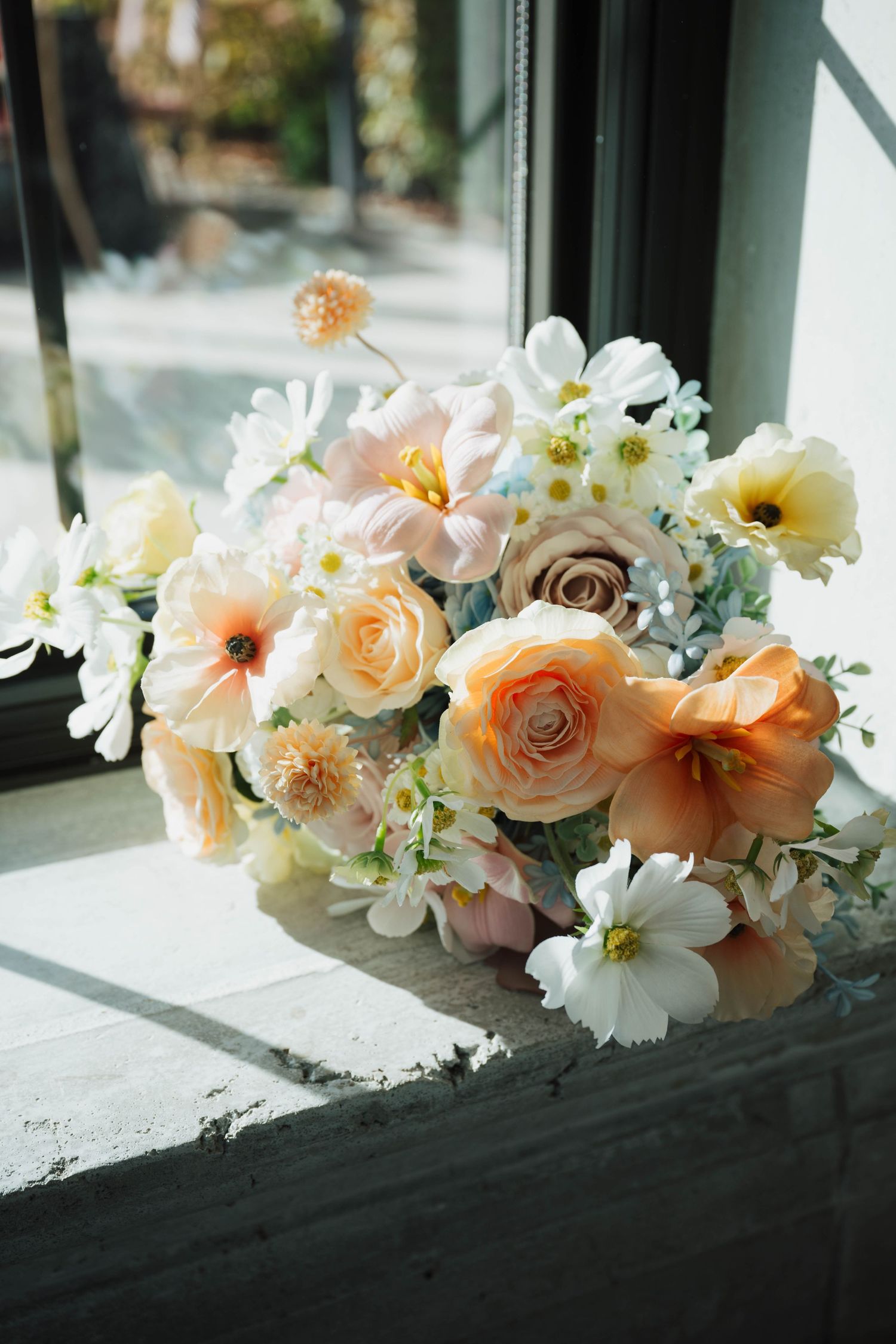 Soft peach and white floral bouquet with roses and cosmos resting on a windowsill in natural light.